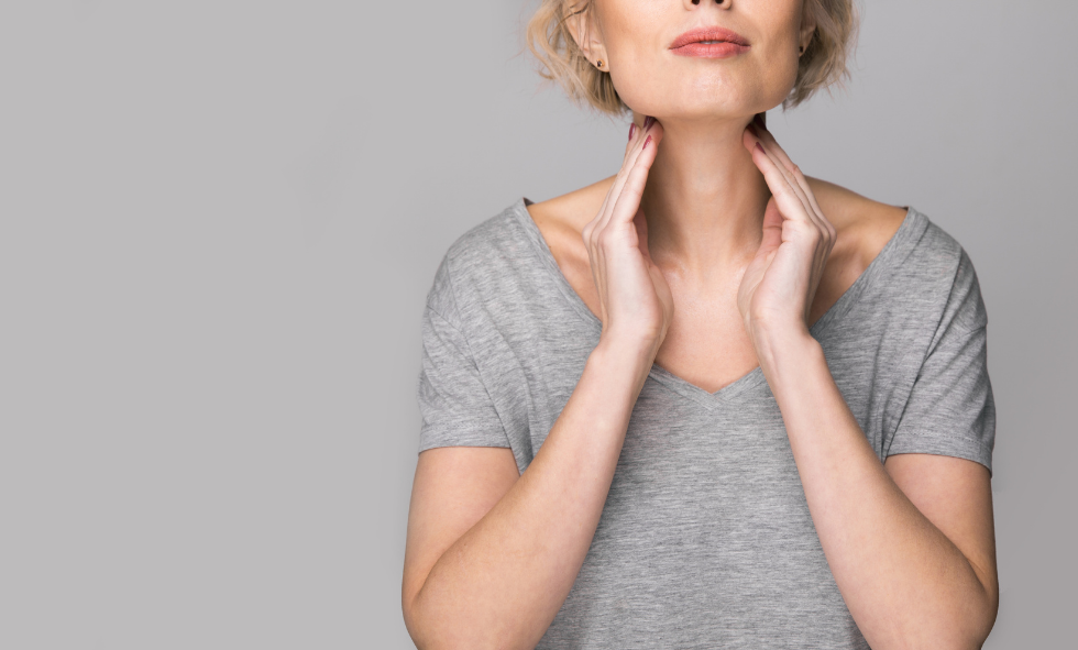 woman in gray t shirt presses both hands against base of chin at neck for thyroid disease